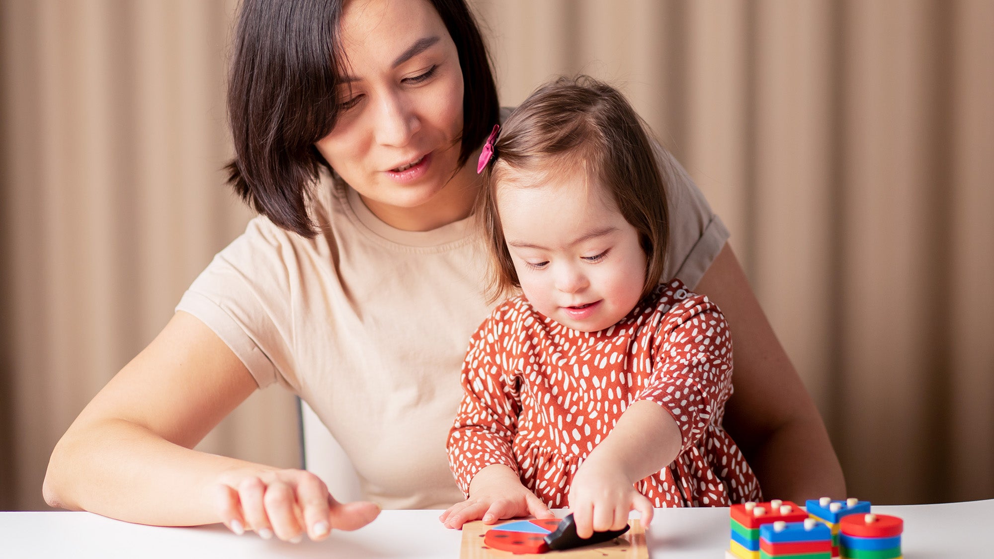 A woman helps her young daughter with Down's syndrome finish a wooden puzzle