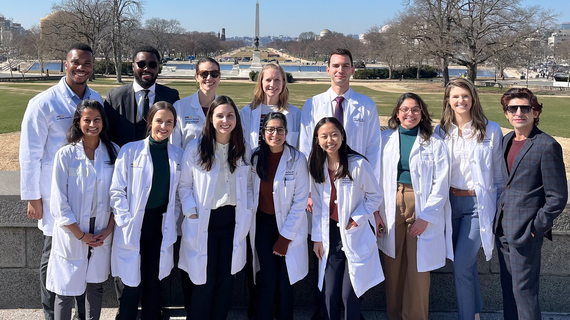 A group of medical residents in white coats stands together on the National Mall with the Washington Monument in the background